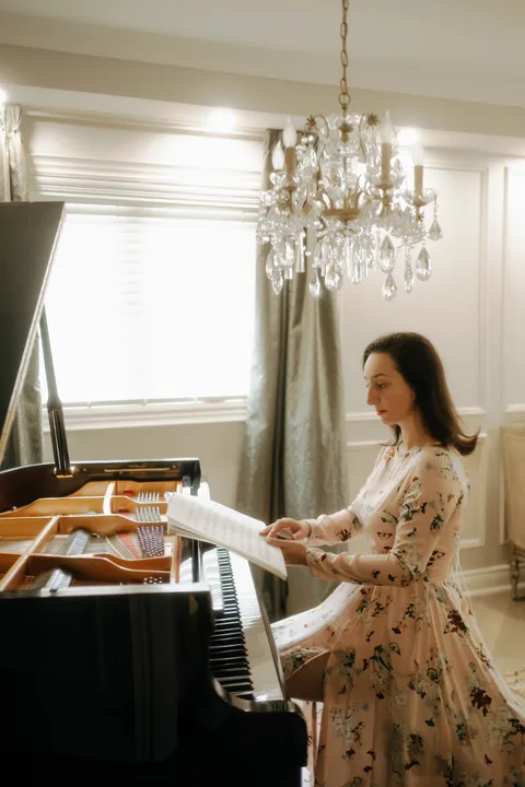 Mekhriban Mamedova reading from an open score at a black grand piano beneath a crystal chandelier.